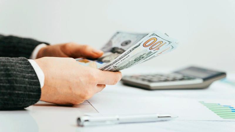 Image of a person's hand counting money with pen and calculator on the background