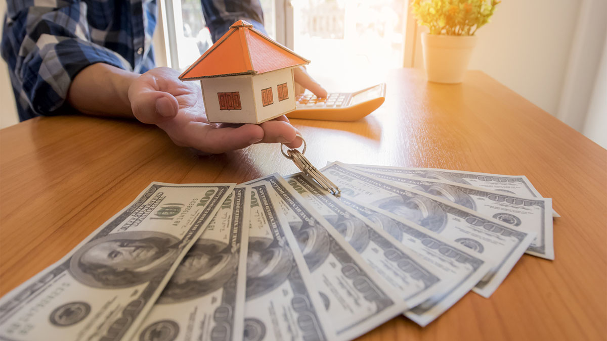 Image of person holding a miniature house and money on the table
