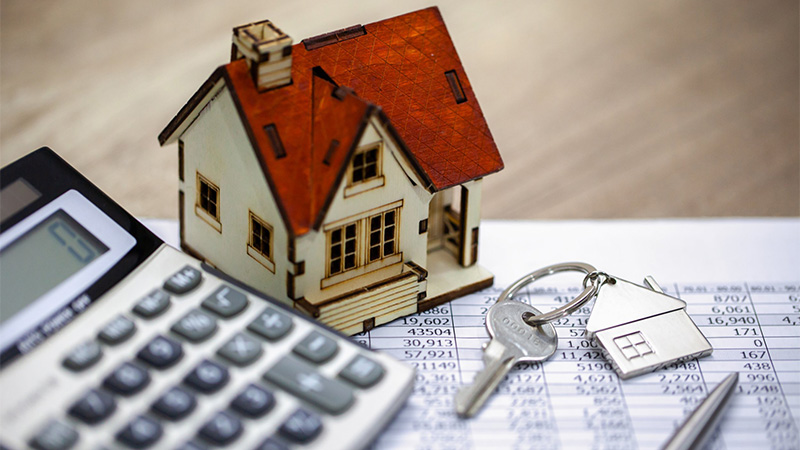 Image of Calculator, house key, and miniature house on top of paper