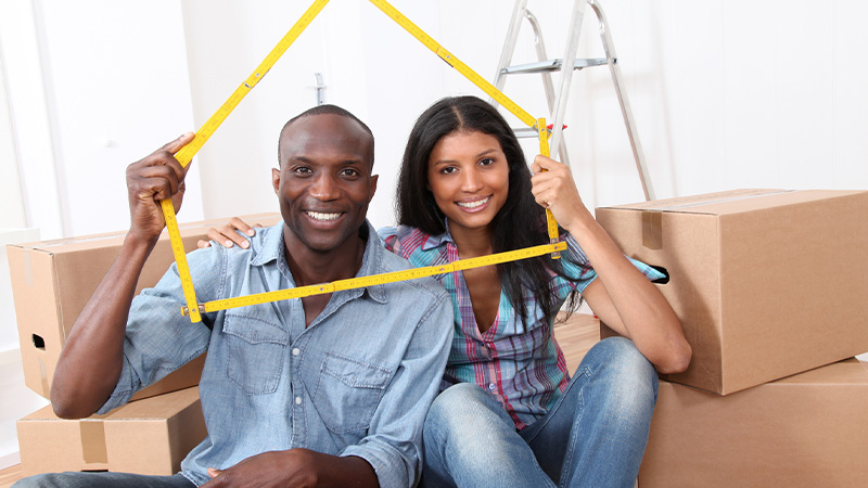 A couple moving to a new house holding a house outline sign.