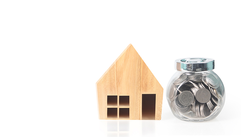 A wooden house model with a bottle of coins