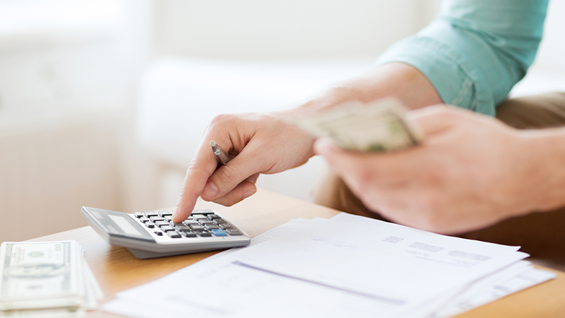 Close up view of a man holding a cash and computing on a calculator