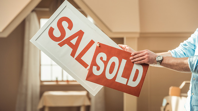 Cropped shot of a man holding a sale and sold signboard