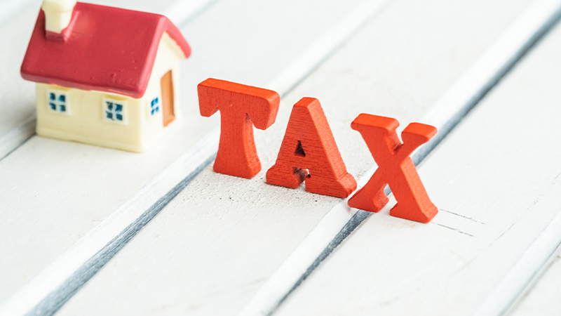 Image of a wooden house model with wooden TAX letters on a table.