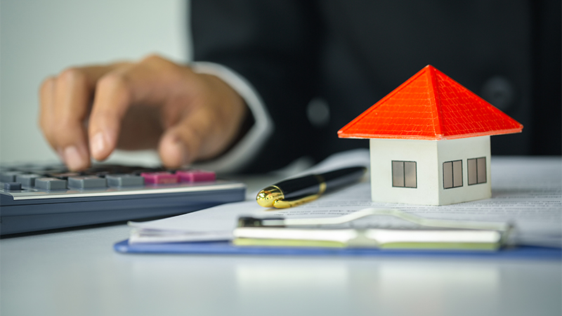 Image of a person using calculator and a toy house on the table